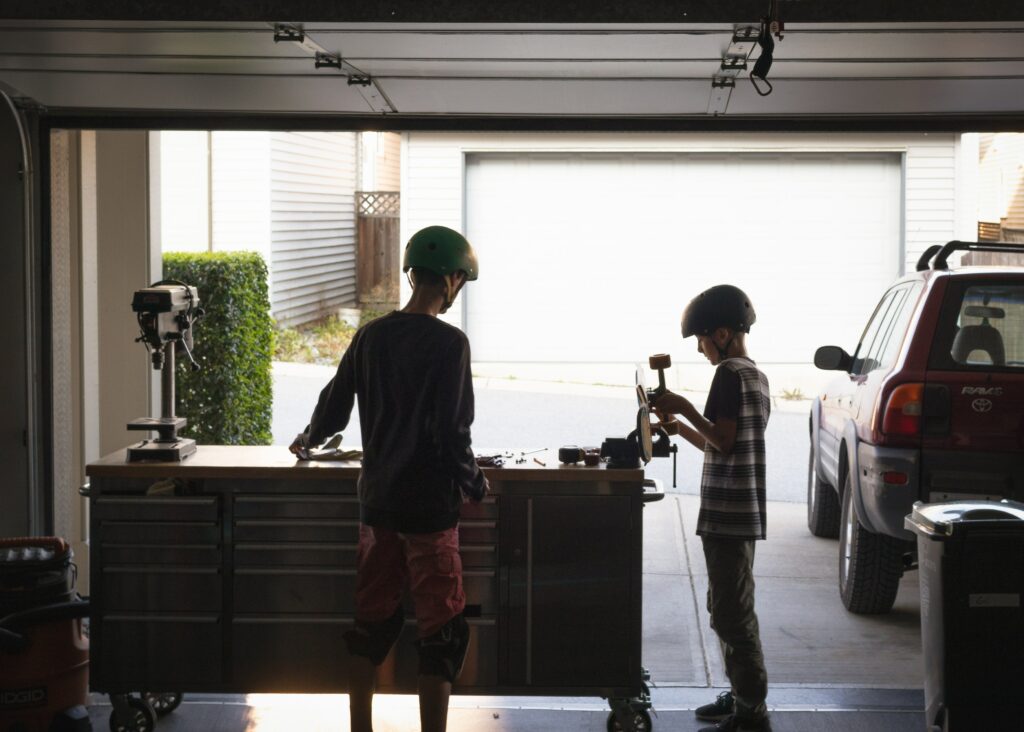 A photo of two boys in a garage working on fixing something, with a text that says “Take your bookings with you anywhere on your mobile with Myslots Scheduling Software”