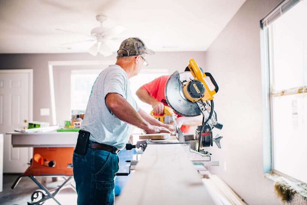 A photo of a man using a saw to cut a long piece of wood in a workshop, with a text that says “Don’t worry about your home services. They are booked and paid online with Myslots Scheduling Software