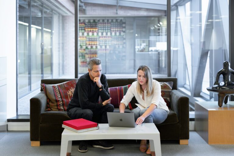 An agent and a client sitting on a couch and using a laptop with Myslots Scheduling App on the screen